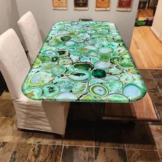 the table is covered with green and blue art work, which has white chairs around it