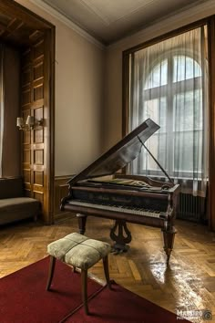 a grand piano sitting on top of a hard wood floor next to a couch and window