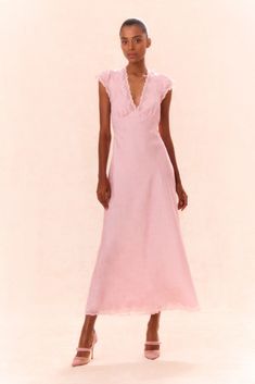 a woman in a pink dress is standing on a white background with her hands behind her back