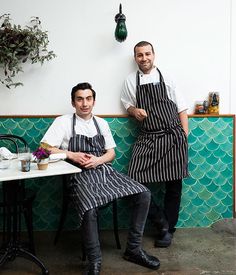 two men in aprons sitting at a table