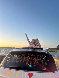 two women sitting on top of a car with the word seniorr written on it