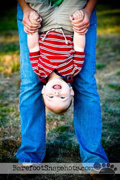 a man holding a baby upside down in the air with his head on another child's back