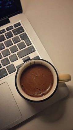 a cup of coffee sitting on top of a laptop computer