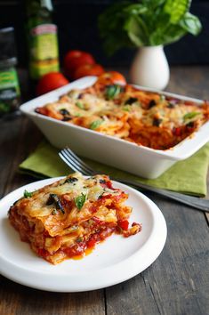 a white plate topped with lasagna next to a casserole dish on a wooden table