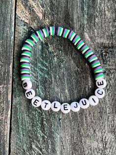 a beaded bracelet with words written in white, green and black beads on a wooden surface