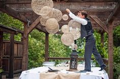 a man standing on top of a table next to a lantern and paper balls hanging from the ceiling