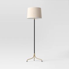 a floor lamp with a white shade on the base and a black metal pole,