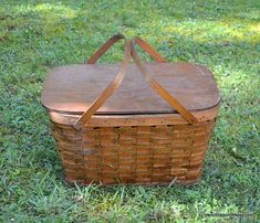 an old picnic basket sitting in the grass with two straps on it's sides