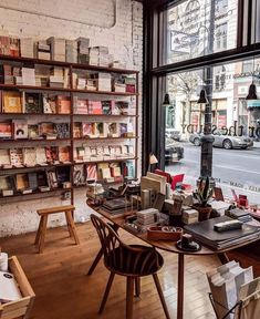 a room filled with lots of books on shelves next to a table and chairs in front of a window