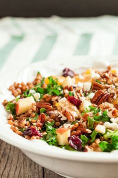 a salad with nuts, cheese and cranberries in a white bowl on a wooden table