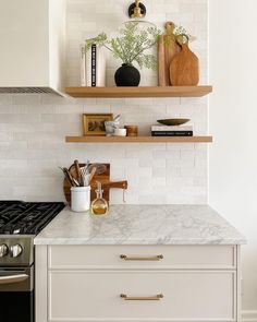 a white kitchen with open shelving above the stove and wooden shelves holding utensils