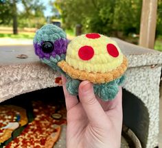 a hand holding a small stuffed animal next to a piece of pizza on a table