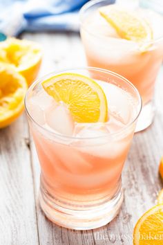 two glasses filled with pink lemonade sitting on top of a table next to sliced oranges