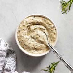 a white bowl filled with cream sauce on top of a marble counter next to a napkin