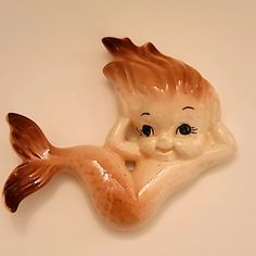 a ceramic figurine of a little mermaid on a white surface with blue eyes