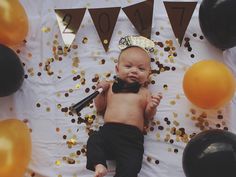 a baby laying on top of a table next to balloons and confetti cones