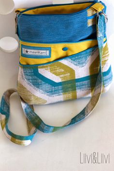 a blue and yellow purse sitting on top of a white table next to a cup