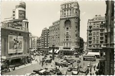 an old black and white photo of a busy city street with cars, buildings, and pedestrians