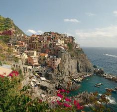 a small village on the edge of a cliff by the ocean with boats in the water