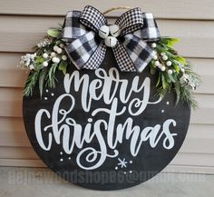 a merry christmas sign hanging on the side of a house with wreaths and bows