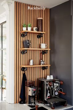 a coffee maker and some cups on a shelf next to a wall with wood slats