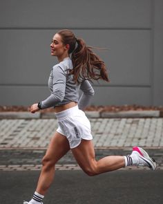 a woman is running on the street with her hair blowing in the wind and wearing white shorts