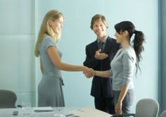 two women and a man shaking hands in front of a table with papers on it