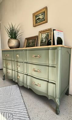 a green dresser with pictures on it and a potted plant