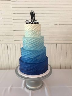 a blue and white ombrella cake with a couple topper sitting on it