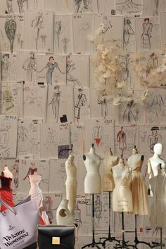 several mannequins and dresses on display in front of a wall covered with drawings