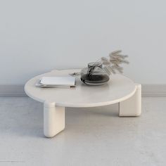 a white coffee table with a plant on top and a book in the middle, sitting against a wall