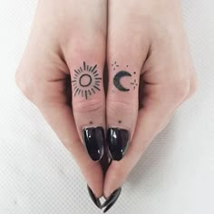 two fingers with sun and moon tattoos on them, one has a black nail polish