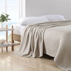 a bed with a blanket on top of it next to a white wall and window