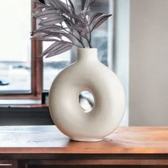 a white vase with a plant in it on top of a wooden table next to a mirror