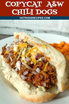 a chili dog with cheese and onions on a white plate next to sweet potato fries