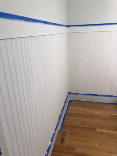 an empty room with white walls and blue tape on the wall, while wood flooring is being painted