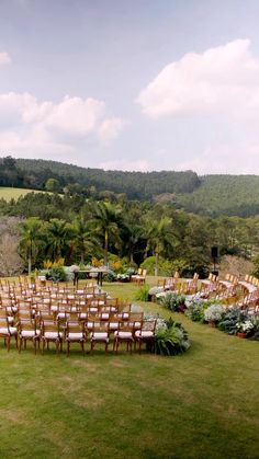 an outdoor ceremony set up with wooden chairs and greenery in the foreground, surrounded by lush green hills