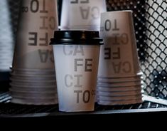 coffee cups sitting on top of a shelf in front of a chain link fence with the words cafe to go written on them