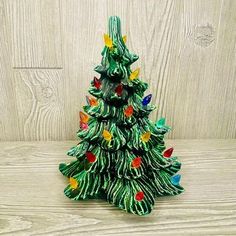 a green ceramic christmas tree with lights on it's base sitting on a wooden surface