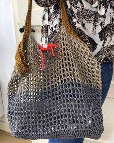 a woman is holding a purse made out of crocheted material and red handles