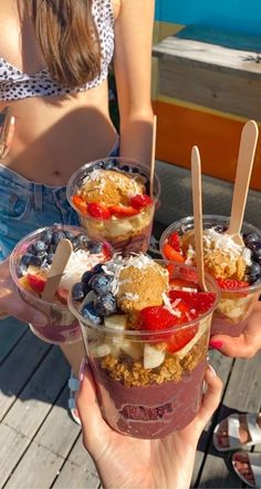 three desserts in plastic cups with strawberries, blueberries and bananas on top