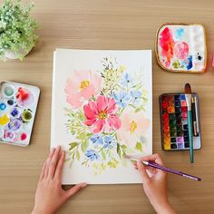 a person is painting flowers on a paper with watercolors and paintbrushes