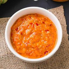 a white bowl filled with sauce on top of a burlied table cloth next to an orange pumpkin