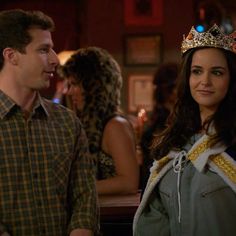 a man and woman standing next to each other in front of a bar wearing crowns