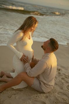 a pregnant woman sitting on the beach with her husband