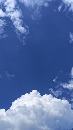 the airplane is flying high in the blue sky with white clouds above it and below