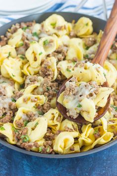 a skillet filled with pasta and meat on top of a blue cloth next to a wooden spoon