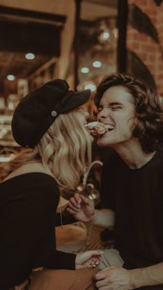 two people sitting at a table with food in their mouth and one person eating something out of his mouth