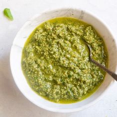 a white bowl filled with pesto sauce and a spoon in the bowl next to it