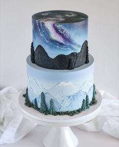 a three tiered cake decorated with mountains and the night sky painted on it's side